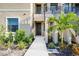 Close-up of the entrance to a condo unit with a small palm tree, black door and colorful landscaping at 23445 Collina Way # 10103, Port Charlotte, FL 33980