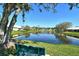 Serene water view of community pond with mature trees and lush green grass with a park bench nearby at 4149 Salernes Ave # 3048, Sarasota, FL 34233