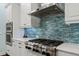 Close-up of a gas cooktop under a vent hood with a blue decorative tile backsplash and white cabinets at 581 Mast Dr, Bradenton, FL 34208
