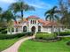 Home featuring barrel tile roof, arched windows and doorway, mature palms and well-manicured lawn and garden at 7934 Royal Birkdale Cir, Lakewood Ranch, FL 34202