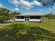 Rear view of a white home with a screened-in porch, green trim, gravel driveway, and lush green grass at 4116 34Th E Ave, Bradenton, FL 34208