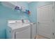 A spacious laundry room with a white washer and dryer, shelf, and a door to the side at 5317 Coral Reef Way, Bradenton, FL 34211