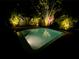 Night view of a backyard pool surrounded by lush, tropical landscaping and subtle lighting at 5802 De Palmas Ave, Holmes Beach, FL 34217
