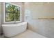 Spa-like bathroom featuring a standalone soaking tub, large window with outdoor views, and sleek marble tiled walls at 115 Solana St, North Port, FL 34287