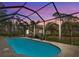 A serene screened-in pool with water features and lush landscaping viewed at twilight at 115 Solana St, North Port, FL 34287