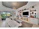 Bright living room with white sofa, custom built-ins with TV, tray ceiling, and sliding glass doors to outdoor space at 5469 Lampiasi St, Sarasota, FL 34238