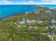 An aerial view showcasing a charming blue house surrounded by lush greenery and stunning ocean views at 691 Gulf Bay Rd, Longboat Key, FL 34228