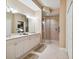 Bathroom with double vanity, framed mirror, walk-in shower with glass doors, and neutral tile flooring at 9441 Discovery Ter # 101A, Bradenton, FL 34212