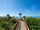 Picturesque wooden boardwalk leading to a beautiful white sand beach with clear blue skies and palm trees at 1211 Gulf Of Mexico Dr # 702, Longboat Key, FL 34228