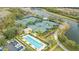 Aerial view featuring tennis courts, a pool, lush landscaping, and a parking lot near a scenic waterway at 7623 Camminare Dr, Sarasota, FL 34238