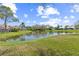 Scenic lake view with lush green lawn, blue skies, and homes in the distance create a tranquil outdoor setting at 3815 Muirfield Ct, Palm Harbor, FL 34685