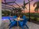 Screened-in patio features a fire pit and ample seating, with a view of the pool and lush landscaping at sunset at 813 Tailwind Pl, Sarasota, FL 34240