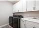 Well-lit laundry room with white cabinets, quartz countertop, sink, and dark front load washer and dryer at 922 Fernleaf Run, Bradenton, FL 34212