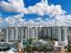 Stunning aerial view of a modern building with a pool and palm trees on the rooftop deck against a bright, cloudy sky at 111 S Pineapple Ave # 918, Sarasota, FL 34236