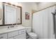 Well-lit bathroom with a white vanity, framed mirror, shower with white curtain, and a commode at 7036 Whittlebury Trl, Lakewood Ranch, FL 34202