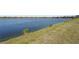 Panoramic water view showcasing a serene lakefront setting with grassy shoreline and neighborhood homes in the distance at 7036 Whittlebury Trl, Lakewood Ranch, FL 34202