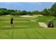 Golfer tees off on a lush green course with a sand trap and golf cart nearby at 5646 Country Lakes Dr, Sarasota, FL 34243