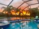 Screened-in pool featuring palm trees, a lake view, and a vivid sunset, perfect for relaxation at 11742 Forest Park Cir, Bradenton, FL 34211