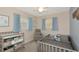 This bedroom features a crib, a comfy gray chair, and two windows dressed with light blue curtains at 5026 Brookmeade Dr, Sarasota, FL 34232