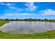 Scenic view of a pond surrounded by lush green grass and neighborhood homes under a bright blue sky at 16111 Sunny Day Dr, Bradenton, FL 34211
