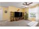 Bright living room with yellow walls, ceiling fan, large TV, and natural light from the window at 4509 Halls Mill Xing, Ellenton, FL 34222