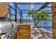 Outdoor kitchen with stainless steel grill and bar top overlooking the pool, lake, and lush landscaping at 7327 Greystone St, Lakewood Ranch, FL 34202