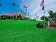 Expansive golf community clubhouse with manicured green lawn and towering palms under a bright blue sky at 8681 Daydream St, Sarasota, FL 34238