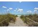 Sandy beach path framed by lush dune grass, leading to the ocean under a bright, partly cloudy sky at 8779 Midnight Pass Rd # 406H, Sarasota, FL 34242