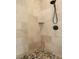 Close-up of bathroom stone tile shower with stone pebble floor and black rainfall shower head at 1930 Bayshore Dr, Englewood, FL 34223