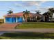 Charming home featuring a well-manicured lawn, a salmon-colored metal roof, and vibrant blue garage doors at 3572 Peace River Dr, Punta Gorda, FL 33983