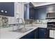 Close-up of a modern kitchen sink, with white countertops, designer backsplash and dark blue cabinets at 6520 Clemson St, Bradenton, FL 34207