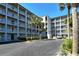 Exterior of a condo with multiple floors and balconies and views of a parking lot, small palm trees, and blue sky at 3108 Lake Bayshore Dr # 211, Bradenton, FL 34205