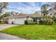 Charming home featuring a lush green lawn, beautiful landscaping, and a white exterior with a tiled roof at 5614 Garden Lakes Dr, Bradenton, FL 34203