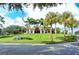 Beautiful exterior of the clubhouse with palm trees, lush green grass, and a vibrant blue sky at 8025 Via Fiore, Sarasota, FL 34238