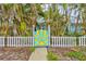 Quaint, vibrant blue home with a charming white picket fence and a sunny gate framed by tropical palm trees at 256 144Th Ave, Madeira Beach, FL 33708