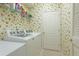 Functional laundry room with modern washer and dryer, wire shelving, and patterned wallpaper at 6103 Aviary Ct, Bradenton, FL 34203