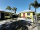 A cheerful yellow waterfront property featuring a red door, patio, and lush tropical landscaping at 9031 Hilolo Ln, Venice, FL 34293