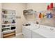 Bright laundry room with built-in shelving, white washer and dryer, utility sink, and organized storage solutions at 1290 Cielo Ct, North Venice, FL 34275