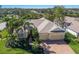 Aerial view of a charming one-story home with a brick driveway, three-car garage, and lush landscaping with palm trees at 8861 17Th Avenue Nw Cir, Bradenton, FL 34209