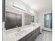 Bright bathroom features double sinks, black cabinets, and tiled shower with view at 7677 Saddle Creek Trl, Sarasota, FL 34241