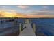 Long wooden dock extends into serene waters, featuring mooring posts, boat lift, and a picturesque sunset backdrop at 2512 Riverside E Dr, Bradenton, FL 34208