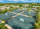 Aerial view of tennis courts with shade structures amidst lush greenery and community buildings at 4852 Peregrine Point N Cir, Sarasota, FL 34231