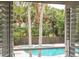 View through plantation shutters of the serene pool area surrounded by lush tropical landscaping at 730 Rellim Ln, Sarasota, FL 34232
