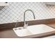 Close up of white porcelain kitchen sink, stainless faucet, dark countertop, and mosaic tile backsplash at 730 Rellim Ln, Sarasota, FL 34232