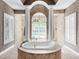 This stunning bathroom features a soaking tub under an arch with natural light and travertine tile at 7921 Waterton Ln, Lakewood Ranch, FL 34202