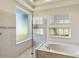 Bright bathroom showcasing a glass enclosed shower, a tub with marble surround and windows for natural light at 742 Shadow Bay Way, Osprey, FL 34229