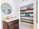 Modern bathroom with a round mirror above the vanity and an open shelving unit at 128 Da Vinci Dr, Nokomis, FL 34275