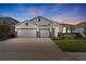 Beautiful single-Gathering home featuring a three-car garage, manicured lawn, and elegant exterior lighting at sunset at 17108 Harvest Moon Way, Bradenton, FL 34211