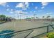 A fenced tennis court with an awning for shade. The backdrop includes a sunny sky and surrounding foliage at 5577 Palmer Cir # 203, Bradenton, FL 34211