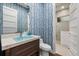 Stylish powder room with unique blue patterned wallpaper, modern sink and vanity, and a glass enclosed shower at 4607 5Th Ne Ave, Bradenton, FL 34208
